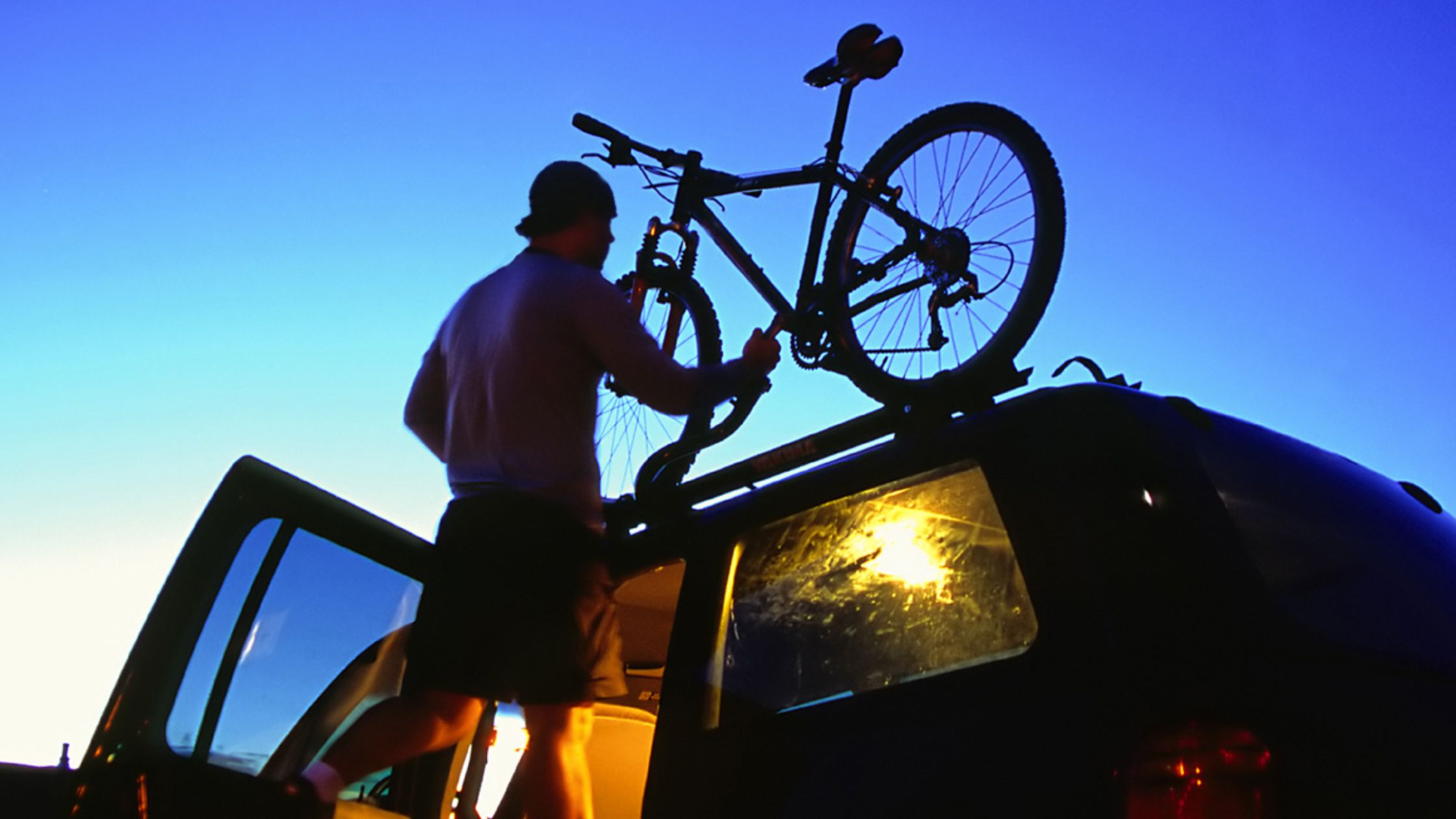 Subaru SUV cargo space. A man places a bike atop his SUV's roof-mounted bike rack.